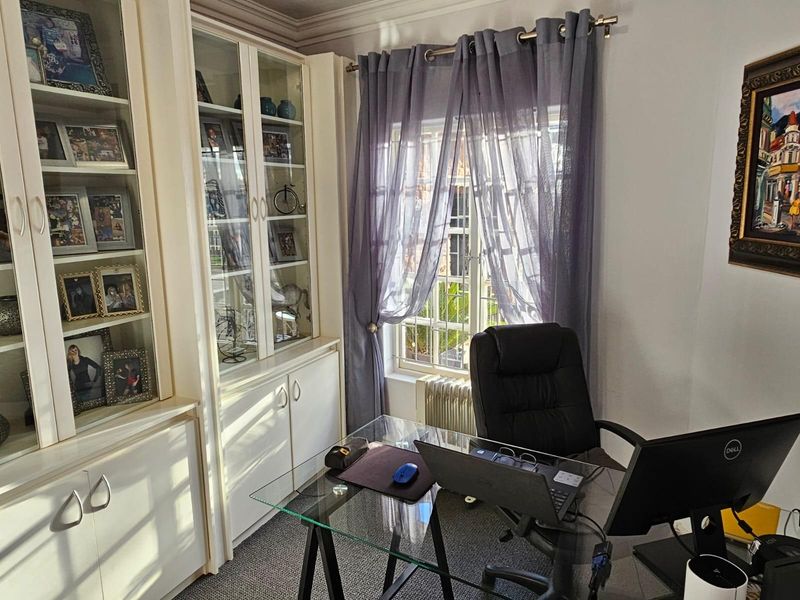 A functional home office featuring built-in floor-to-ceiling cabinetry with glass-fronted display shelving and a window with natural light.