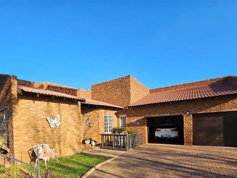 A charming face-brick house exterior featuring a double garage, paved driveway, and a small front patio area under a tiled roof.