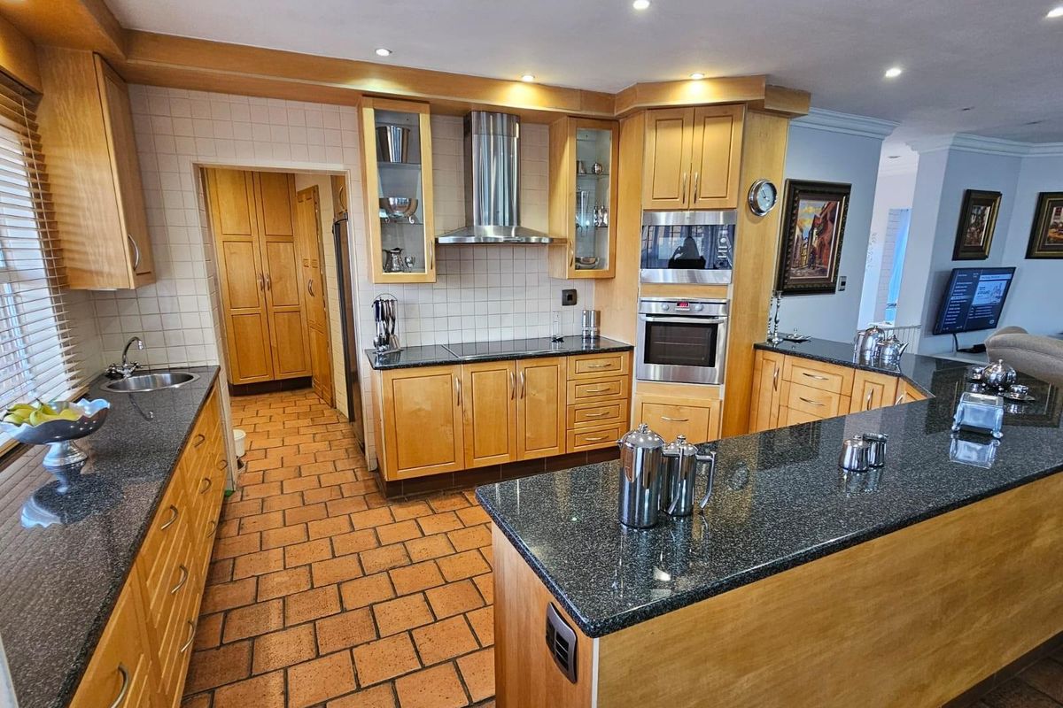 Spacious kitchen featuring light wood cabinetry, dark granite countertops, built-in oven, extractor fan, and terracotta floor tiles with an adjoining scullery area.