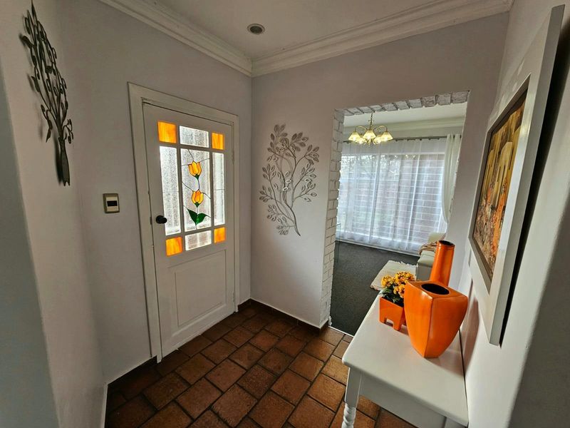 A welcoming entrance hall featuring terracotta floor tiles, a decorative stained-glass front door, and an open archway leading into the living area.