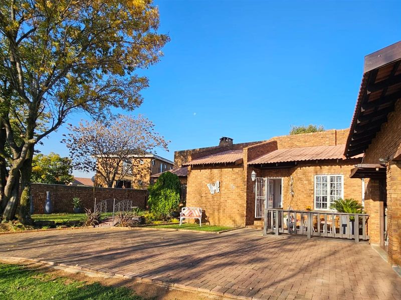 A view of the rear exterior featuring a brick facade, paved courtyard area, and established garden surroundings.