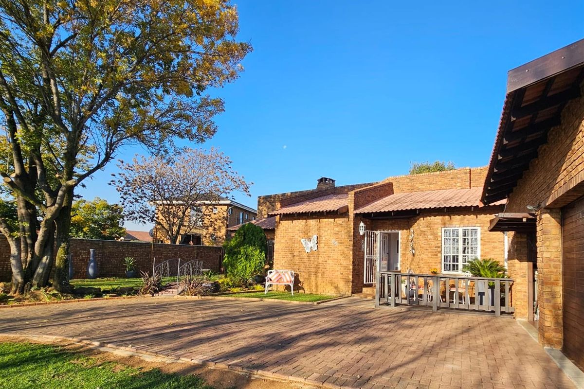 A view of the rear exterior featuring a brick facade, paved courtyard area, and established garden surroundings.