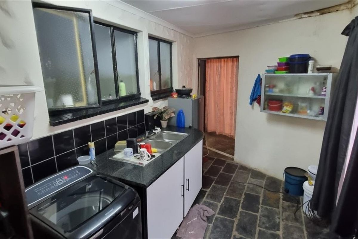 A functional kitchen area featuring a double sink, stone countertops, black tile splashback, and slate flooring, requiring cosmetic updates and ceiling repairs.