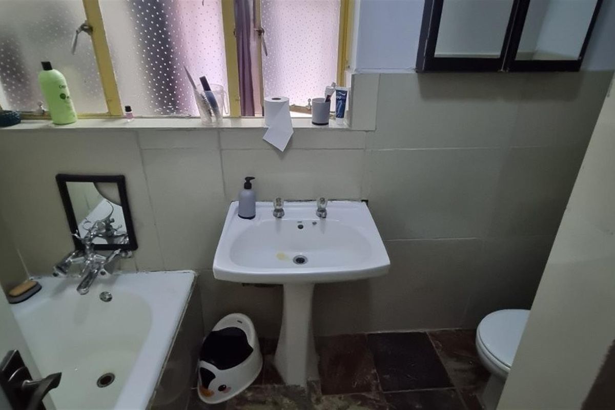 A functional bathroom featuring a pedestal basin, bathtub, and toilet with tiled finishes, offering potential for modernization and cosmetic updates.