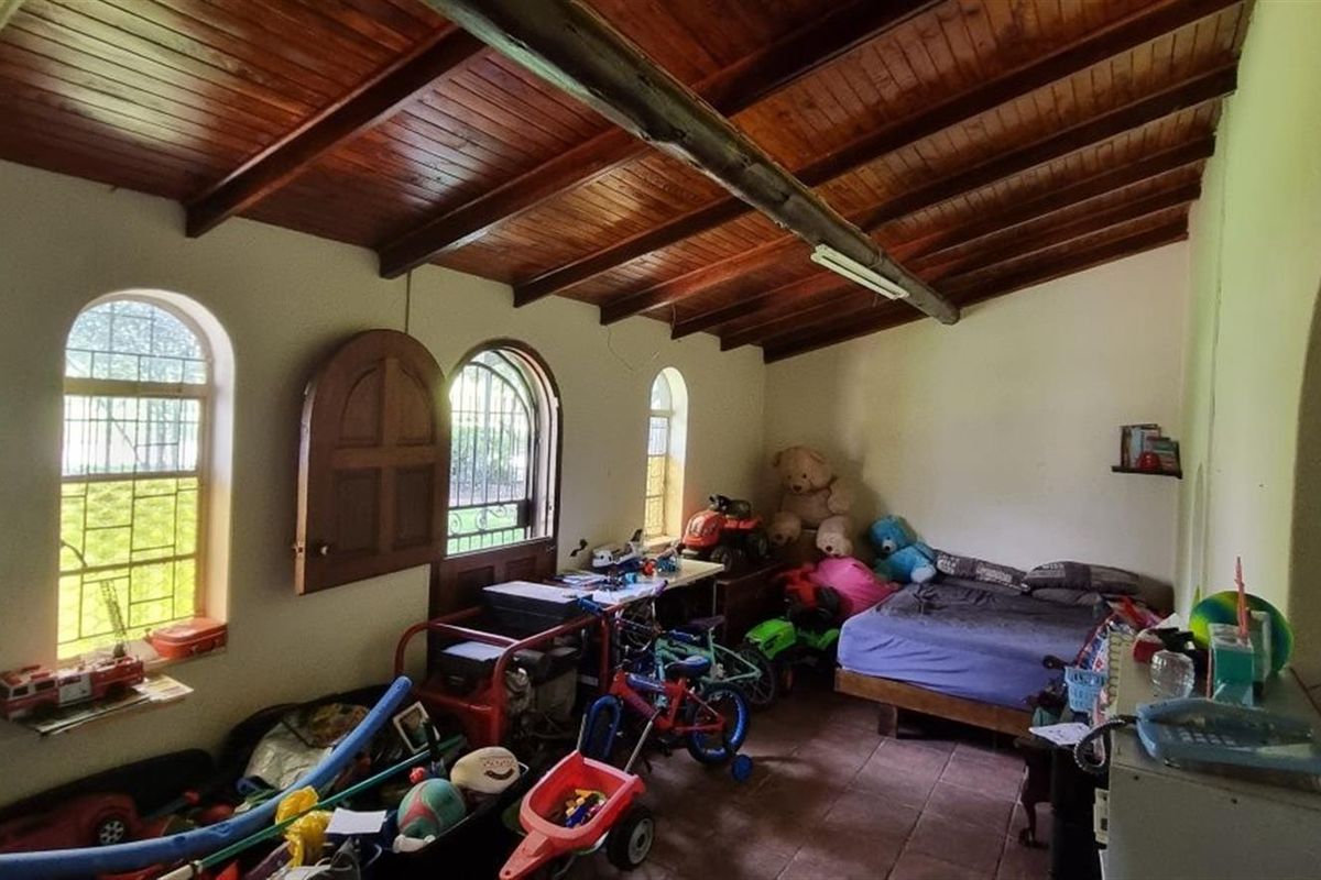 A bedroom featuring a rustic exposed timber beam ceiling, arched windows, and tiled flooring, offering a unique architectural character in need of cosmetic updates.