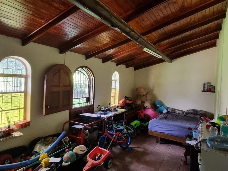 A bedroom featuring a rustic exposed timber beam ceiling, arched windows, and tiled flooring, offering a unique architectural character in need of cosmetic updates.