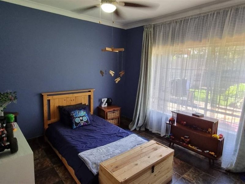 A well-lit bedroom featuring tiled flooring, a ceiling fan, and a large window with curtains, providing a comfortable and functional living space.