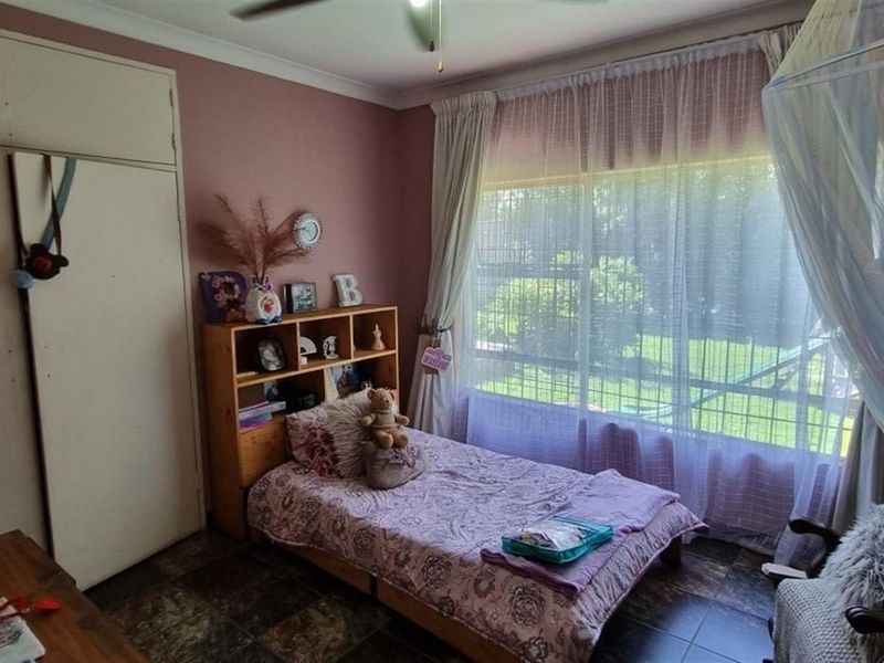 A bedroom featuring tiled flooring, a built-in wardrobe, a ceiling fan, and a large window allowing natural light.