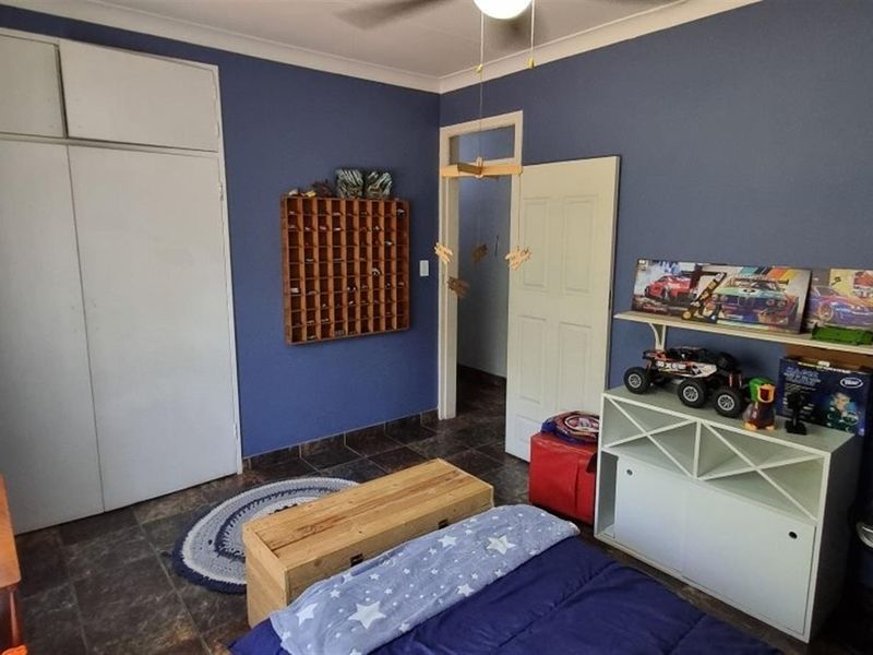 A bedroom featuring tiled flooring, built-in cupboards, and a ceiling fan, finished with blue painted walls.
