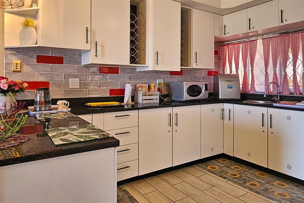 A functional kitchen featuring white cabinetry, dark granite countertops, and a decorative tiled backsplash with red accents.