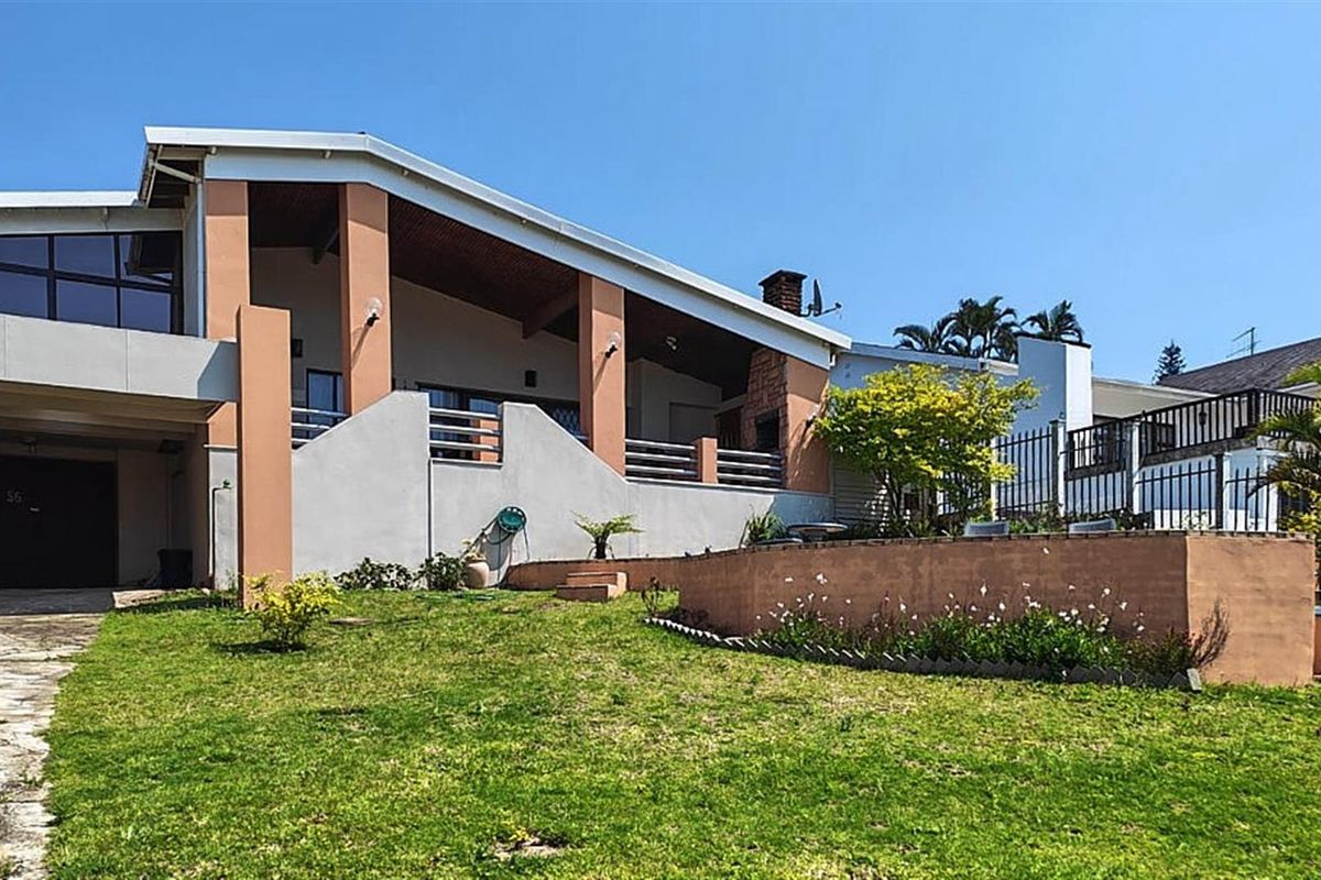A rear view of the property featuring a covered patio area, brick chimney, and a landscaped garden with a retaining wall.