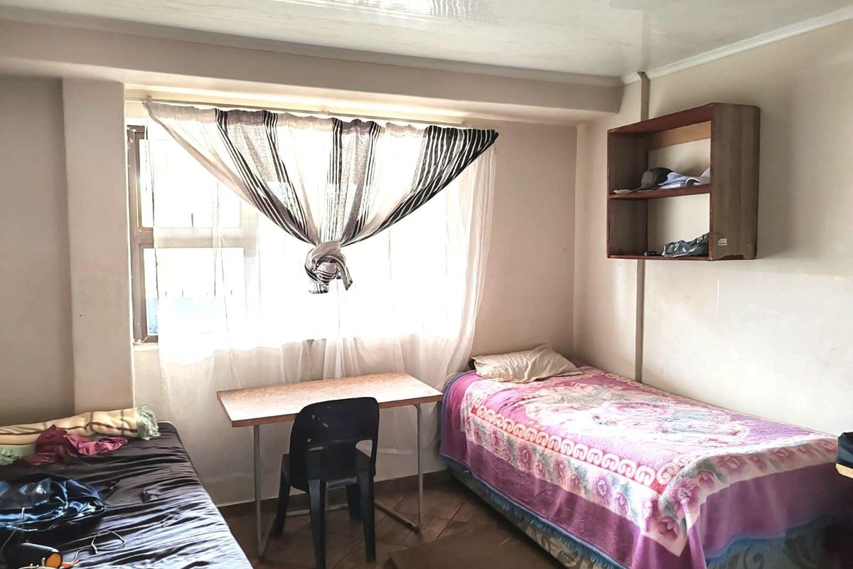 A functional bedroom featuring tiled flooring and a built-in wall-mounted shelving unit, offering a practical layout for residential or commercial accommodation use.