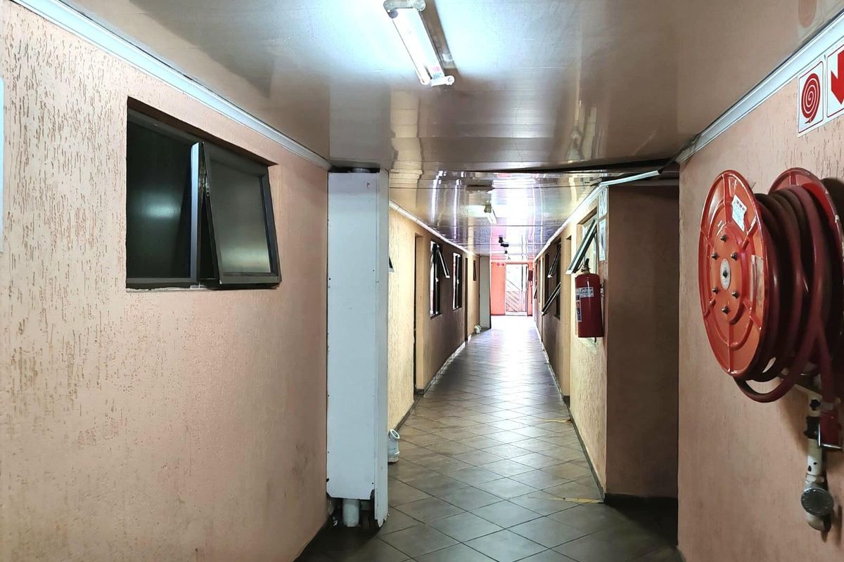 A commercial hallway featuring tiled flooring, fire safety equipment, and fluorescent lighting, showing signs of wear on the wall surfaces.