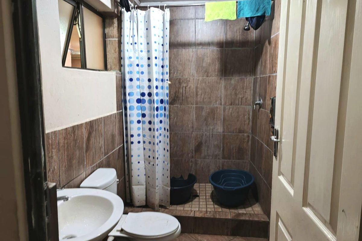 A compact bathroom featuring a shower area, pedestal basin, and toilet with brown wall and floor tiling.