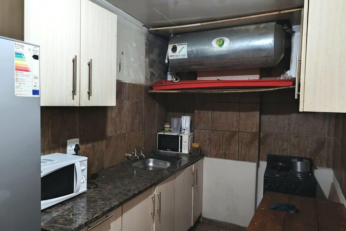 Compact kitchen featuring laminate cabinetry, granite-look countertops, and an exposed electric geyser unit requiring cosmetic finishing.