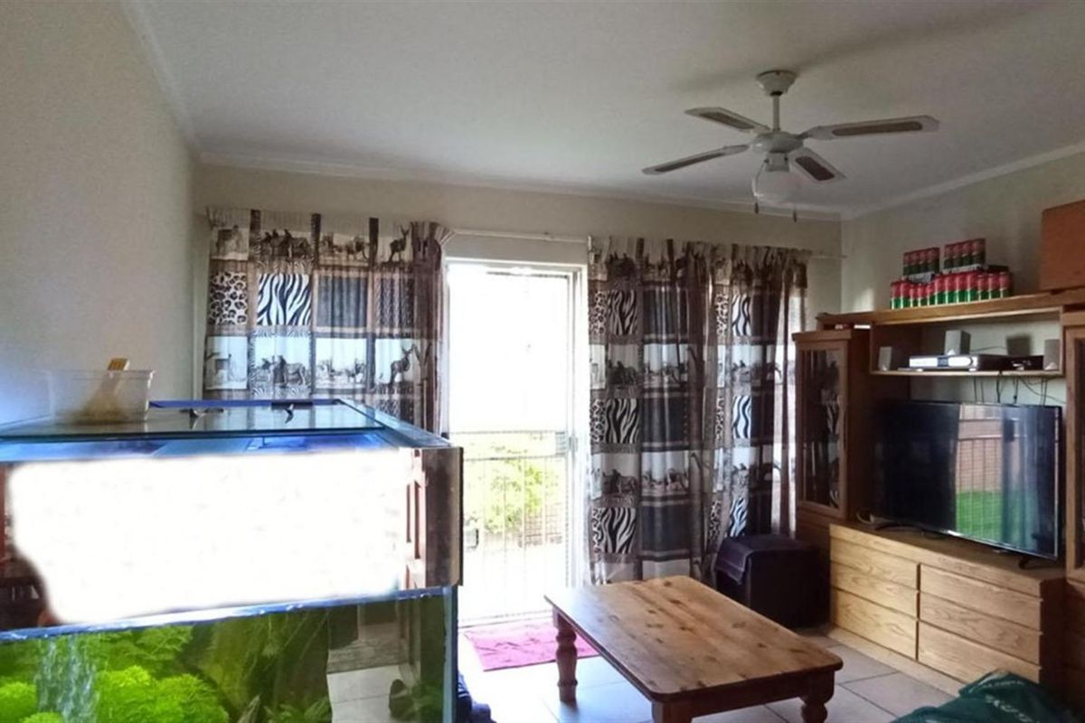 A living room area featuring tiled flooring, a ceiling fan, and a glass door providing access to an outdoor space.