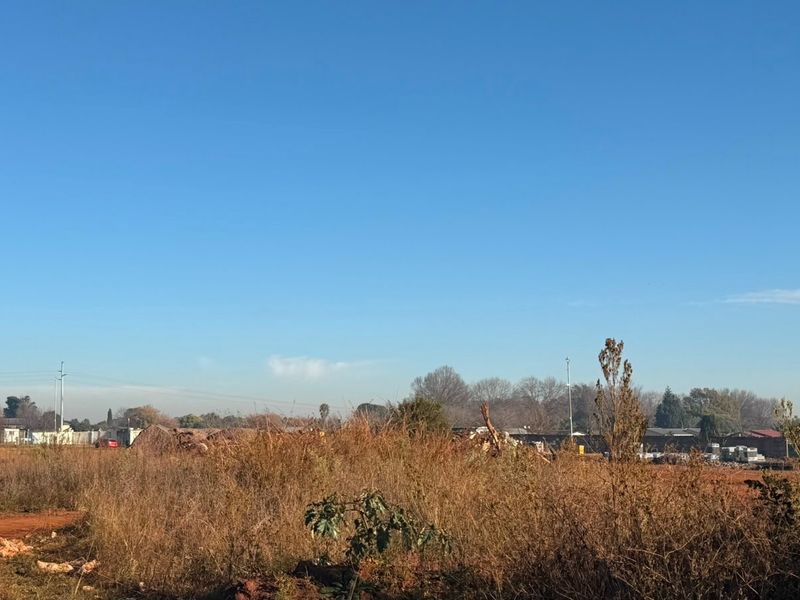 A wide-angle view of an undeveloped industrial plot featuring open land and natural vegetation under a clear blue sky.