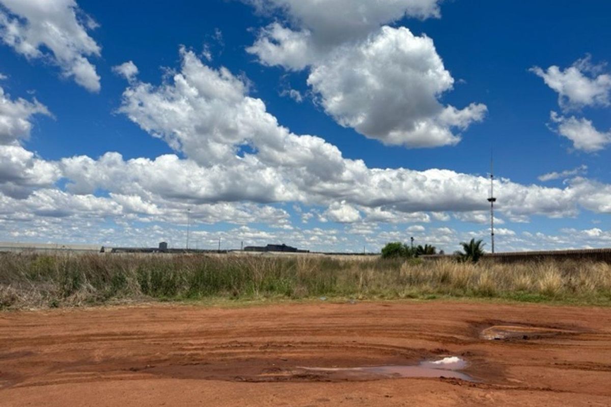 An expansive, unpaved industrial plot featuring open ground, perimeter fencing, and distant industrial structures under a clear sky.