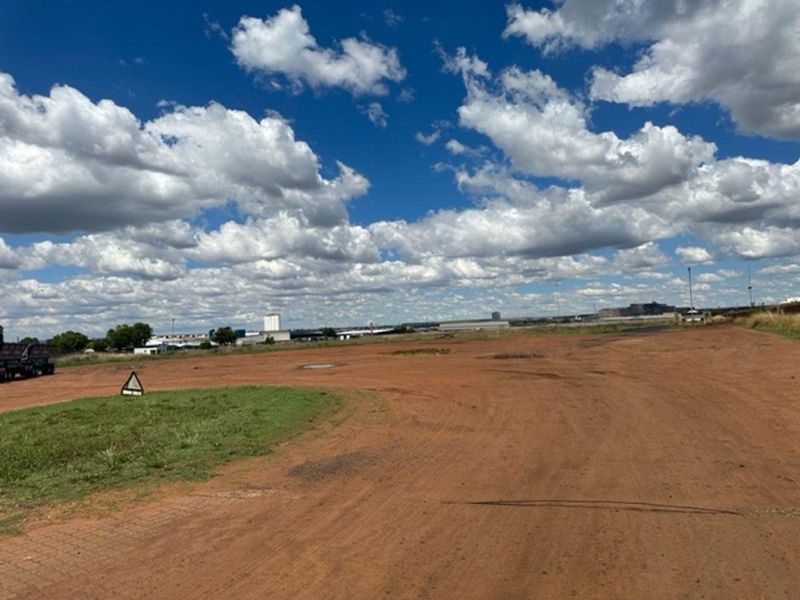 A wide, unpaved industrial plot of land with a grass verge, offering significant space for development or storage.