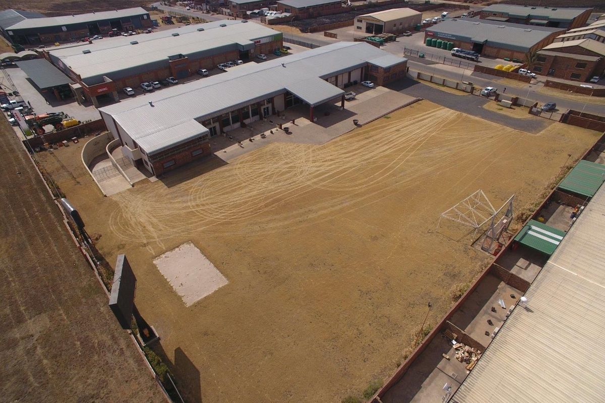 Aerial view of an industrial property featuring a large warehouse building, expansive yard space, and surrounding commercial infrastructure.