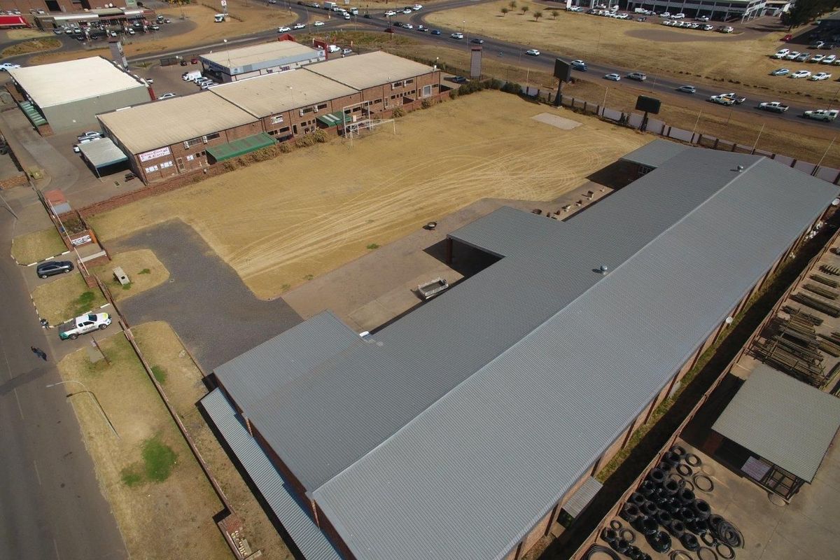 Aerial view of an industrial property featuring a large warehouse building with a metal roof, expansive yard space, and paved access areas.