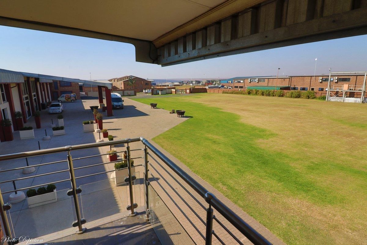Elevated view from a balcony overlooking a paved industrial courtyard and a large, well-maintained grass lawn area.