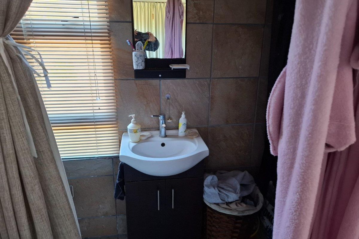 A functional bathroom vanity area featuring a wall-mounted basin, dark cabinetry, and tiled wall finishes with a window providing natural light.