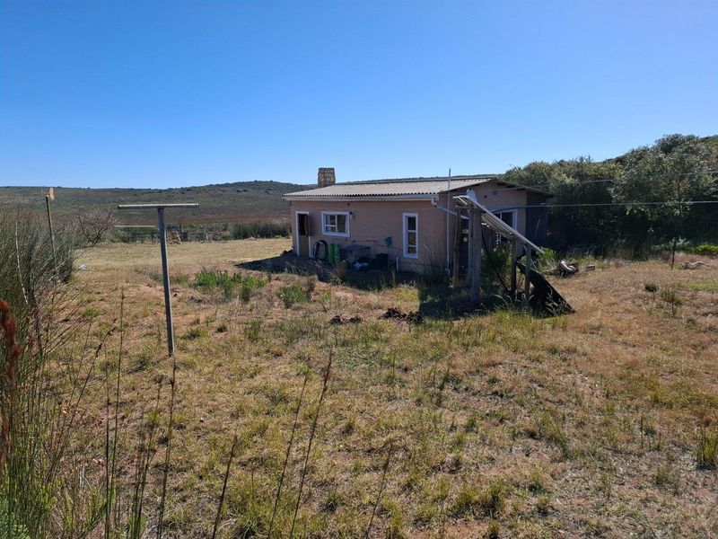 A view of the rear exterior of a farm dwelling, featuring a simple structure set within a large, open rural landscape.
