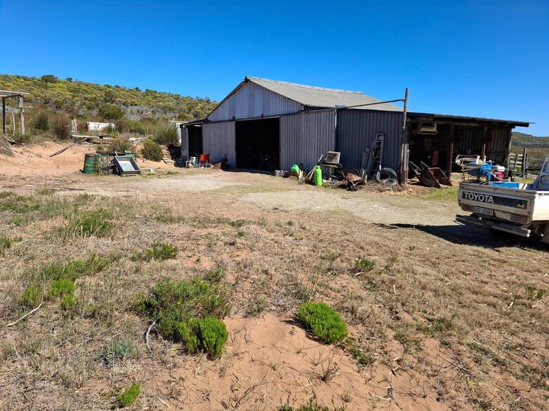 A functional farm shed with corrugated metal cladding and a large open bay, situated on a rural property with surrounding natural landscape.