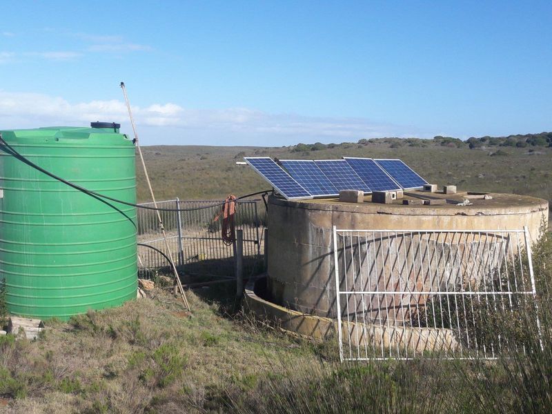 Farm water infrastructure featuring a large green plastic storage tank, a concrete reservoir, and solar panels for off-grid water pumping.