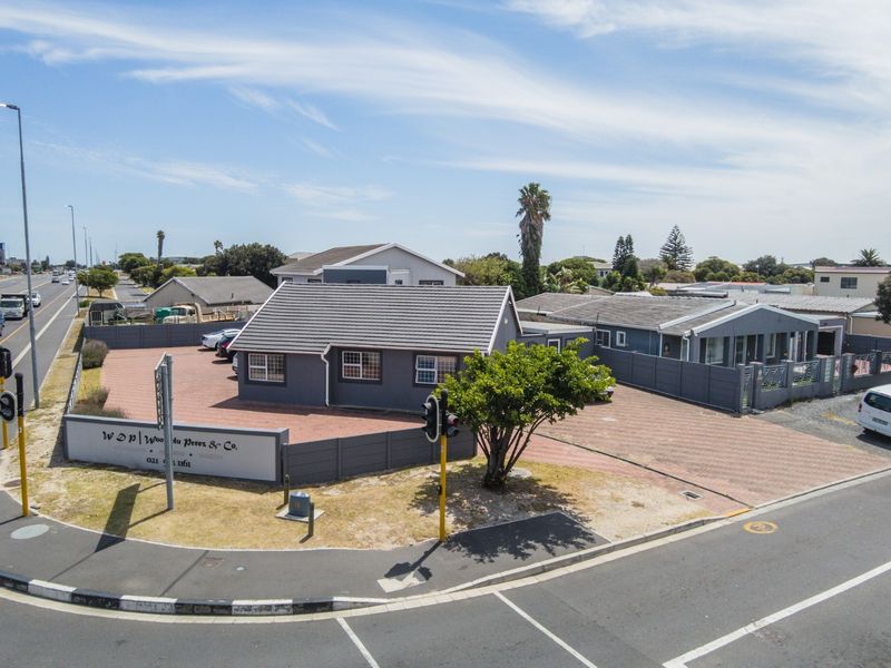 Aerial view of a commercial office property featuring a paved driveway, boundary wall, and tiled roof structure situated on a corner lot.