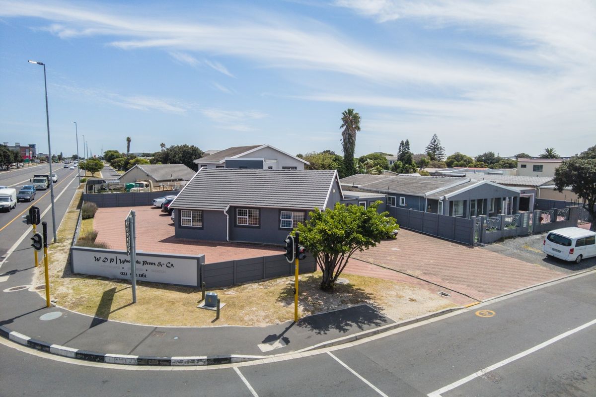 Aerial view of a commercial office property featuring a paved driveway, boundary wall, and tiled roof structure situated on a corner lot.