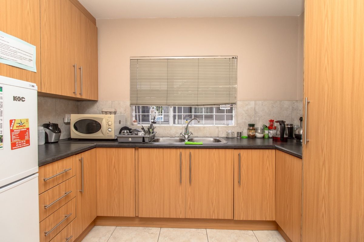 A functional kitchen featuring light wood-finish cabinetry, dark laminate countertops, a stainless steel double sink, and tiled flooring.