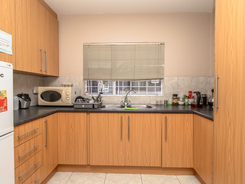 A functional kitchen featuring light wood-finish cabinetry, dark laminate countertops, a stainless steel double sink, and tiled flooring.
