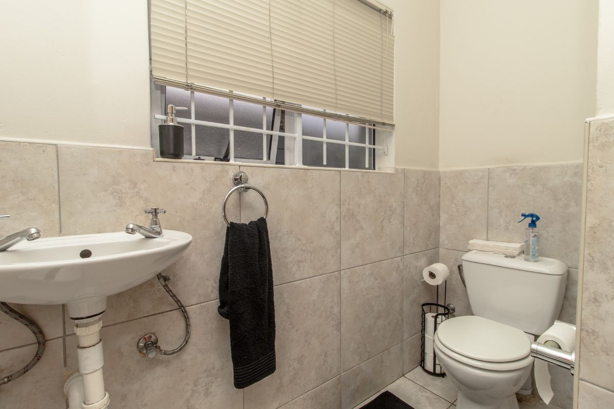 A functional bathroom featuring neutral ceramic wall tiling, a pedestal washbasin with chrome fixtures, and a standard toilet.