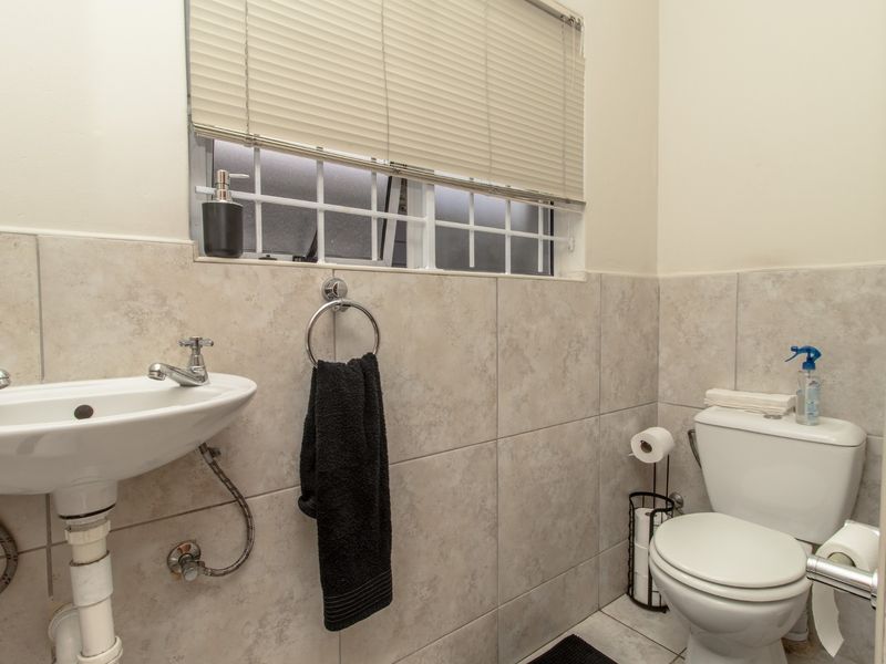 A functional bathroom featuring neutral ceramic wall tiling, a pedestal washbasin with chrome fixtures, and a standard toilet.
