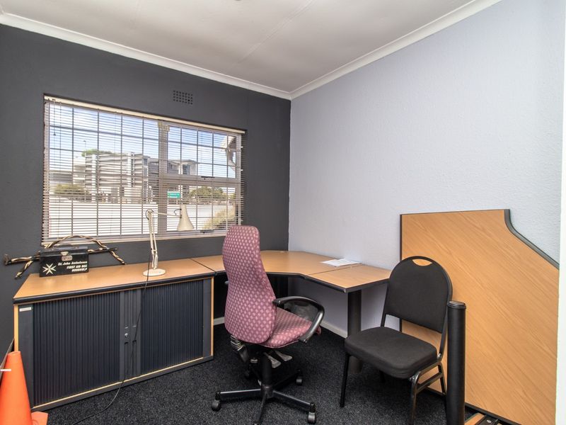 A functional office space featuring dark accent walls, fitted window blinds, and neutral carpeting, suitable for a professional work environment.
