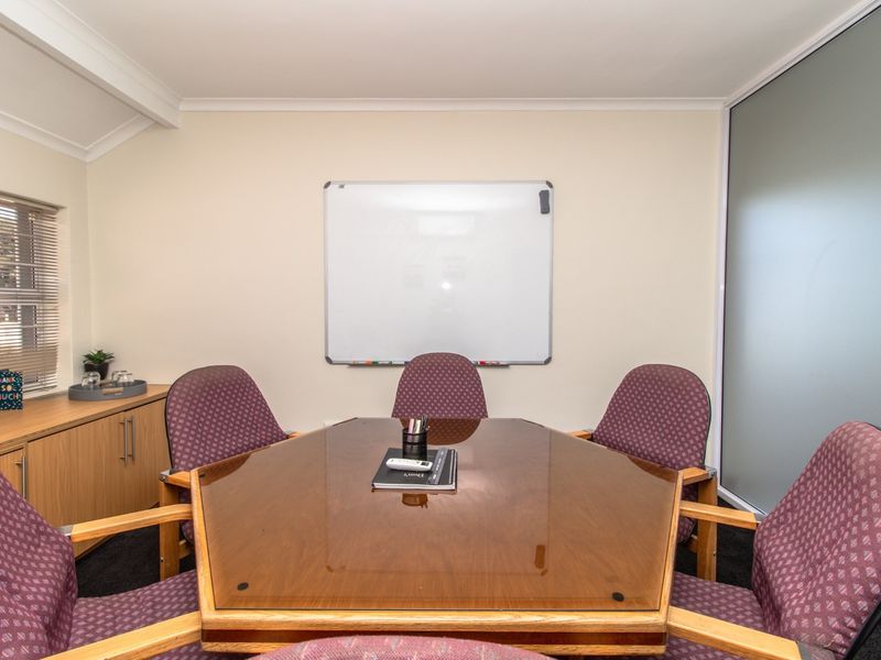 A functional office meeting room featuring built-in cabinetry, a wall-mounted whiteboard, and a frosted glass partition for privacy.