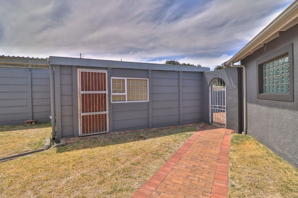 Rear exterior view showing a paved walkway, security gates, and a precast concrete boundary wall.