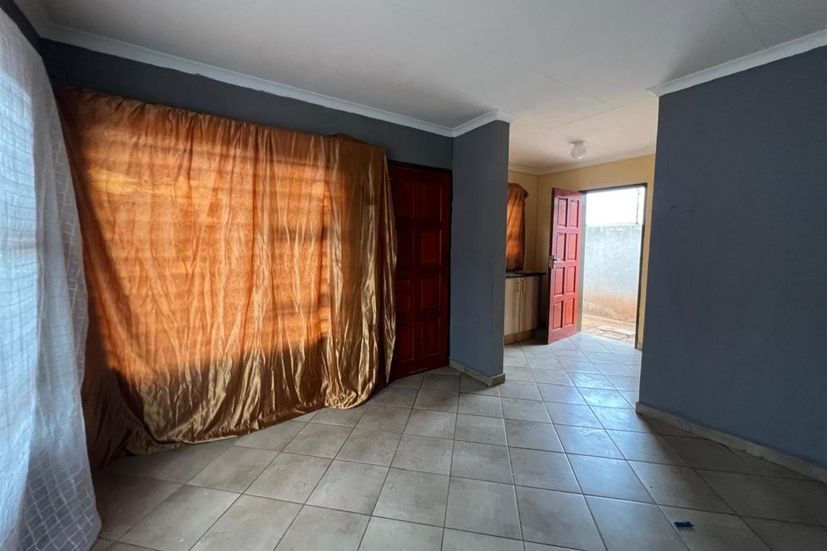A living area featuring tiled flooring, neutral grey walls, and direct access to an exterior doorway.