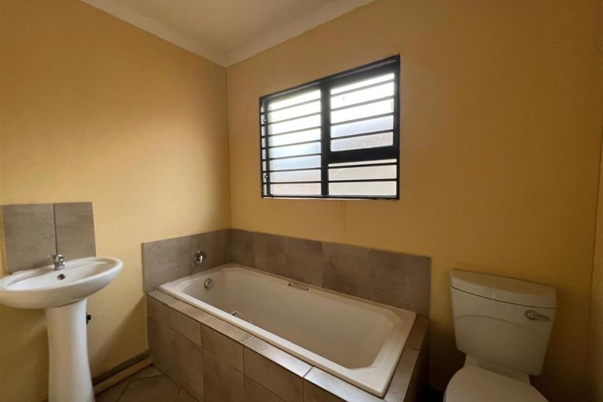 A functional bathroom featuring a pedestal basin, a tiled bathtub, and a toilet, with a window providing natural light.
