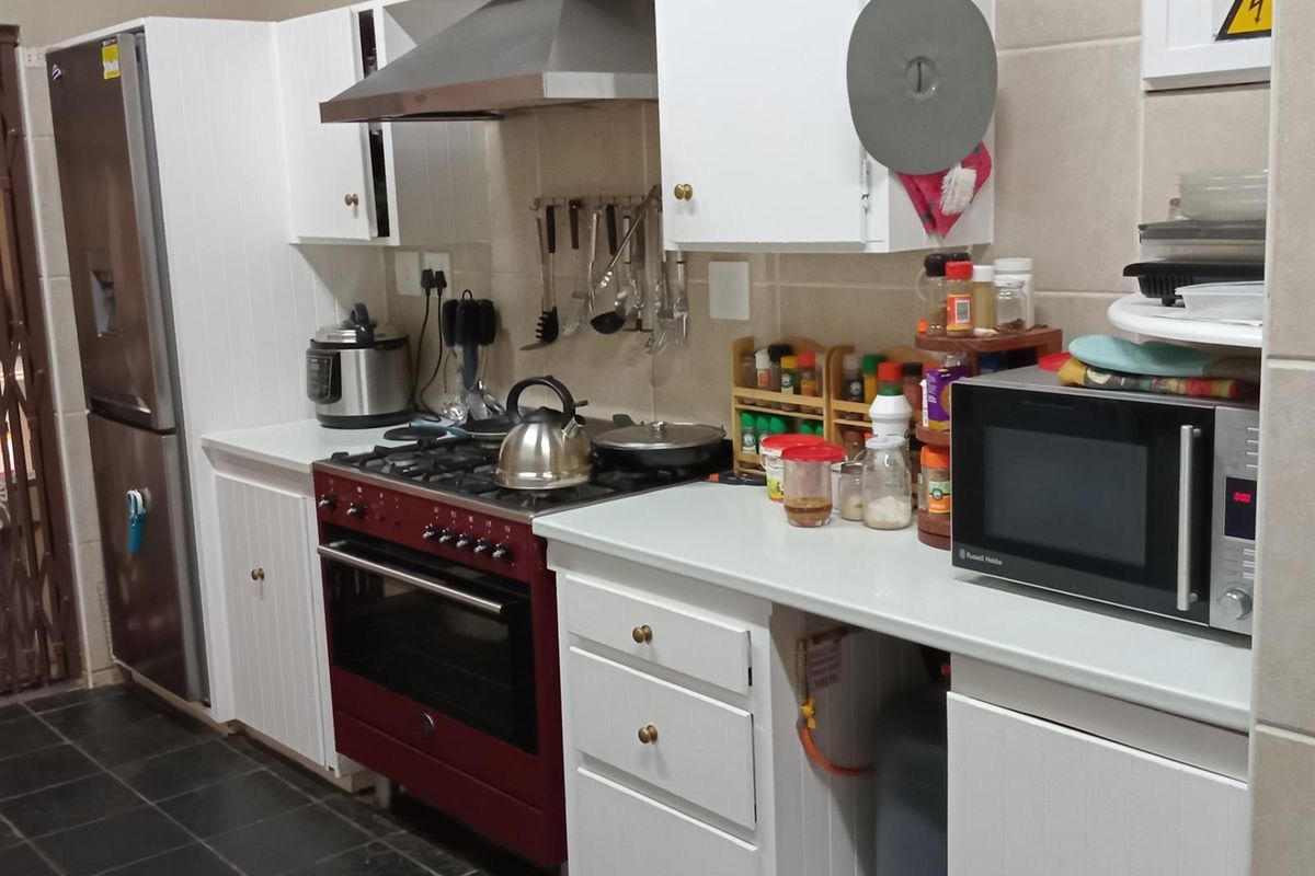 A functional kitchen featuring white cabinetry, a contrasting red freestanding gas stove with extractor fan, and dark tiled flooring.