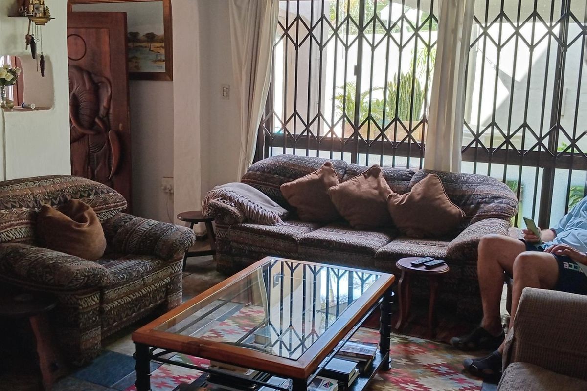 A comfortable living room featuring tiled flooring and large windows secured with metal security gates, providing natural light and access to the exterior.