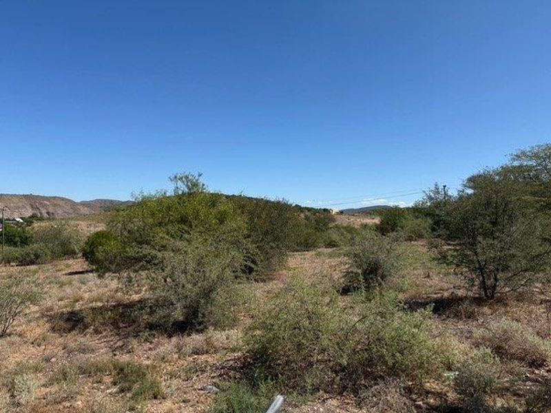 A view of the vacant residential land featuring natural vegetation and a sloped landscape under a clear blue sky.