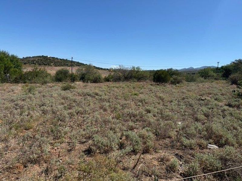 A view of a vacant residential plot featuring native scrub vegetation and distant hilly landscape under a clear blue sky.