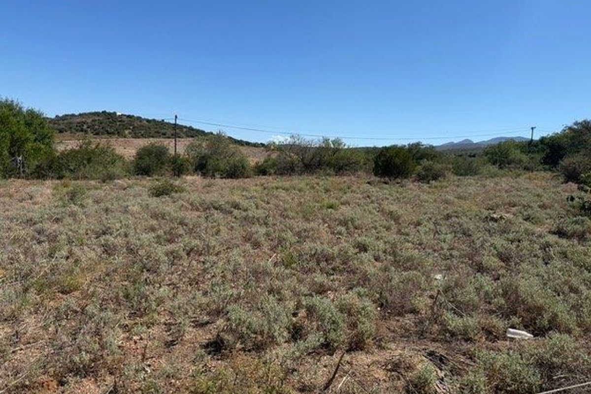 A view of a vacant residential plot featuring native scrub vegetation and distant hilly landscape under a clear blue sky.