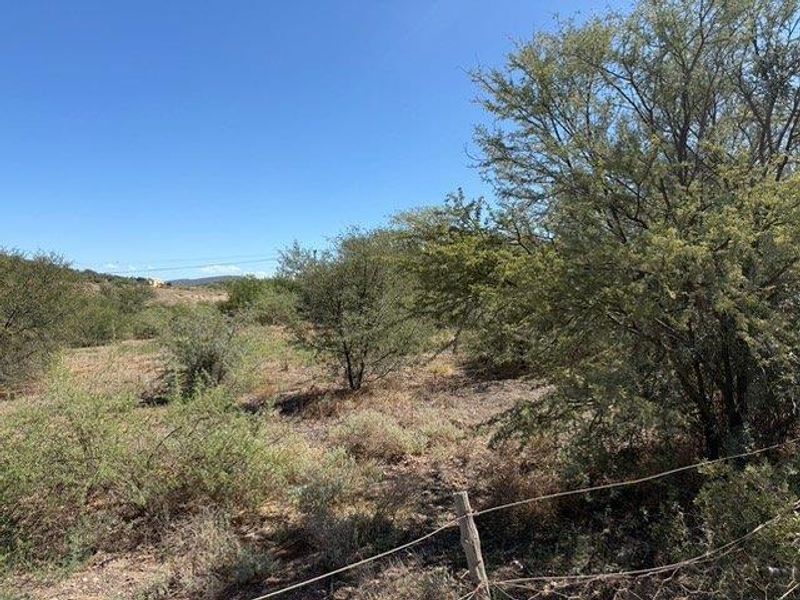 A view of a vacant residential plot featuring native vegetation and wire fencing, offering a natural landscape setting.