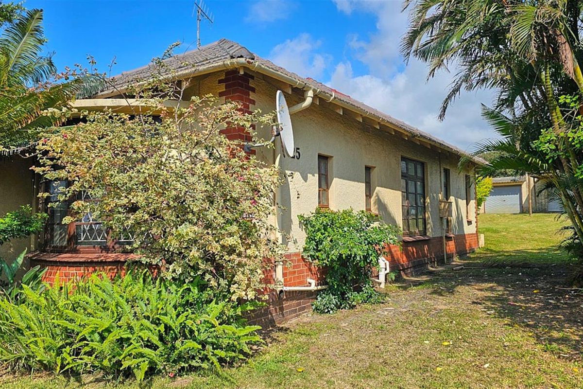 Side view of a traditional house featuring brick and plaster exterior walls, tiled roof, and established garden surroundings.