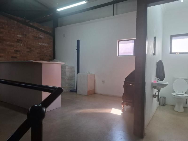 Open plan commercial space featuring exposed brickwork, industrial steel beams, concrete flooring, and an adjacent private restroom facility.