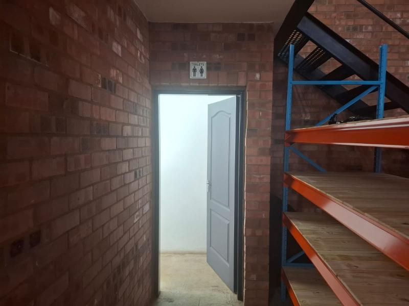 Industrial style hallway featuring exposed brick walls, a metal staircase, and built-in industrial shelving, leading to a restroom area.